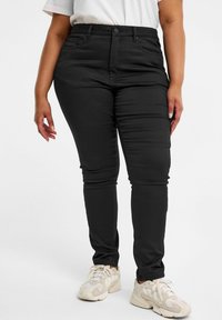 Svarta skinny jeans med knäppning, sidofickor och en slät yta, kombinerade med ljusa sneakers.