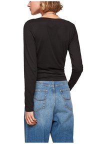 Schwarzes Langarmshirt aus weichem Stoff, taillierter Schnitt, kombiniert mit hellblauen, hochgeschnittenen Jeans mit Gesäßtaschen und Nähten.