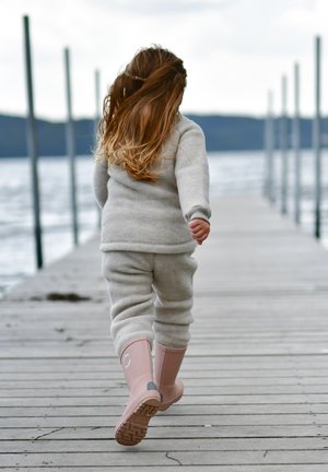 Sivi flis pulover in hlače, obuti v svetlo roza gumijaste škornje, sprehajanje po lesenem pomolu ob vodi. Dolgi, valoviti lasje padajo po hrbtu.