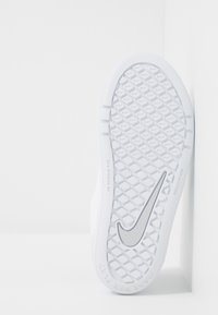 Biała podeszwa sportowego obuwia z teksturowanym wzorem gumowym, z logo Nike w kolorze srebrnym i konstrukcją antypoślizgową. Czyste linie i minimalistyczny styl.