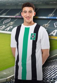 Camiseta blanca con rayas verticales en negro y verde, con un escudo del equipo en el lado izquierdo del pecho. El fondo muestra el interior de un estadio.