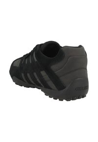 Scarpa sportiva nera caratterizzata da una combinazione di materiali lisci e testurizzati, con un tallone imbottito, una suola flessibile e un brand discreto.