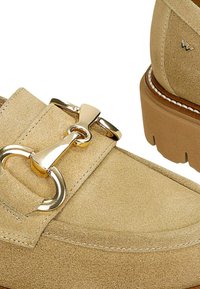 Beige Wildleder-Loafers mit einer auffälligen goldfarbenen Schnalle und einem klobigen Absatz mit strukturiertem Sohlen. Enthält eine Ziernaht entlang der Kanten.