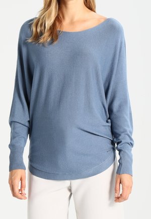 Hellblauer, locker geschnittener Pullover mit weitem Ausschnitt und überschnittenen Schultern. Weiche Textur, gerippte Bündchen und ein abgerundeter Saum.
