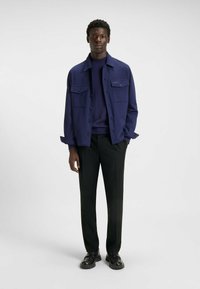 Mørkeblå skjortejakke med to brystlommer over en matchende sweater, parret med sorte bukser og sorte loafers. Glat tekstur.