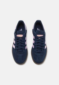 Mørkeblå semskede sneakers med rosa striper, rund tå, flate skolisser og en brun gummisåle. Gullmerke på tungen.