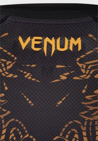 Μαύρο αθλητικό πουκάμισο με υφή, με πορτοκαλί γραφικά και τη λέξη «VENUM» σε στιλιζαρισμένη γραμματοσειρά στο πάνω μέρος της πλάτης.
