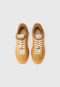 Baskets en daim beige avec lacets blancs et doublure en fausse fourrure, estampillées "Scotch & Soda Amsterdam" sur la languette, vues de dessus sur fond blanc.