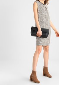 Ärmlös mönstrad klänning med rund halsringning, i kombination med en svart clutchväska och beige ankelstövlar med klack.