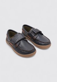 Zapatos de cuero negros con costuras naranjas, una correa de velcro, puntera redondeada y una suela de goma marrón claro con un patrón texturizado.