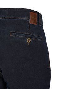 Ciemnoniebieskie dżinsy mają brązową skórzaną łatę na tylnej części pasa i mały żółty guzik na tylnej kieszeni.