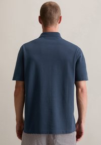 Marineblauw polo-shirt met korte mouwen en een subtiele textuur, voorzien van een klassieke kraag en zijsplitten voor meer bewegingsvrijheid.