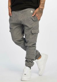 Gray fleece joggers with cargo pockets, tapered cuffs, and a small logo on the back. Paired with white sneakers.