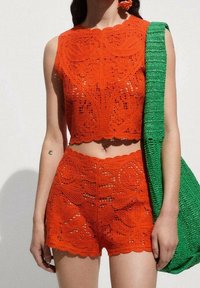 Ensemble deux pièces en crochet de couleur orange vif comprenant un crop top sans manches et un short taille haute à motifs floraux. Accompagné d'un sac vert.