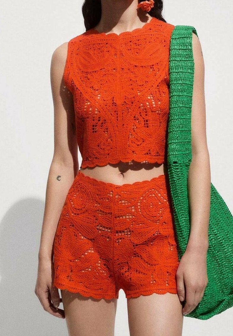 Ensemble deux pièces en crochet de couleur orange vif comprenant un crop top sans manches et un short taille haute à motifs floraux. Accompagné d'un sac vert.