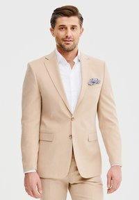 Beżowy lniany garnitur o dopasowanym kroju, jednorzędowa marynarka, biała koszula i wzorzysty poszetka. Gładka tekstura, minimalne detale.