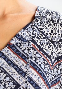 Tissu à motifs bleu marine et blanc avec des dessins floraux et rayés. Matière légère avec un col en V et une texture subtile.