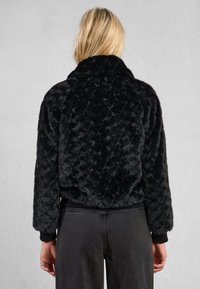 Giacca nera in pelliccia sintetica con texture trapuntata, taglio corto e polsini a costine. Presenta un design con colletto alto per calore e stile.