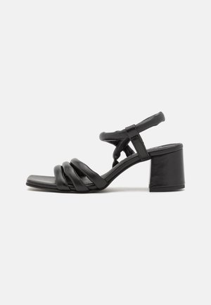 Sandale en cuir noir avec trois brides avant rembourrées, une bride de cheville et un talon bloc moyen sur fond blanc.