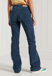 Pantalones de pana de campana azul oscuro con cintura alta, que cuentan con dos bolsillos traseros y un parche de cuero en la pretina.