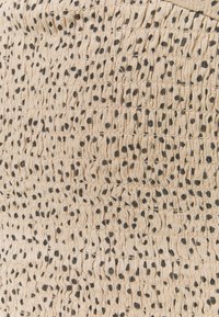 Beige tekstureret stof med sorte pletmønstre; har sammentrukne sektioner, der skaber en bølgende effekt. Tråd er synlig i et område.