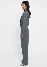 Grijze, cropped blazer met gestructureerde schouders, gecombineerd met op de taille reagerende, op maat gemaakte broeken. Glad stof met subtiele textuur.