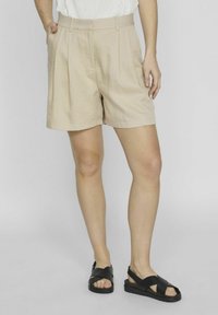 Béžové upravené šortky vyrobené z lehkého materiálu, se skládanými předními částmi, bočními kapsami a uvolněným střihem. Spárovány s černými sandály.
