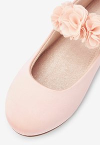 Lyserøde balletflade med en glat stofoverflade, rund tå og dekoration af stofblomster på stropperne. Blød, glitrende inderside.
