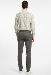 Camisa de manga larga a cuadros en beige claro y verde, combinada con pantalones con estampado en gris carbón. Zapatillas blancas con detalles en verde azulado.