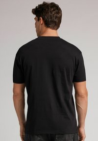 Schwarzes T-Shirt mit kurzen Ärmeln aus weichem Stoff. Es hat einen klassischen Rundhalsausschnitt und eine normale Passform, ohne sichtbare Muster oder Hardware.