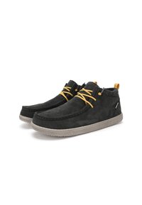 Zapatos casuales de ante negro con suelas grises, cordones amarillos, cuellos de tobillo de punto y tiradores sobre un fondo blanco.
