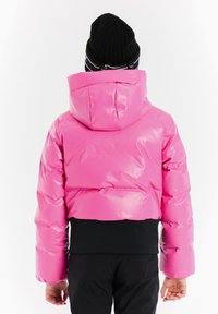 Gekürzte Pufferjacke in glänzendem, knalligem Rosa mit Kapuze, ausgestattet mit einem schwarzen unteren Saum und taillierten Ärmeln. Strukturierten, mattschwarzen Hosen sichtbar.
