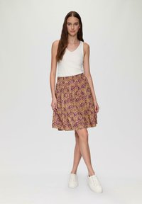 Blumiger Rock in Gelb- und Lilatönen, aus leichtem Stoff. Weißes Tanktop mit V-Ausschnitt, kombiniert mit weißen Sneakers.