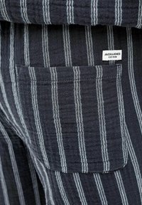 Marine-stribet stof med tynde hvide linjer. Har en sidelomme og et mærketag, der står "JACK & JONES EST.1990." Struktureret overflade.