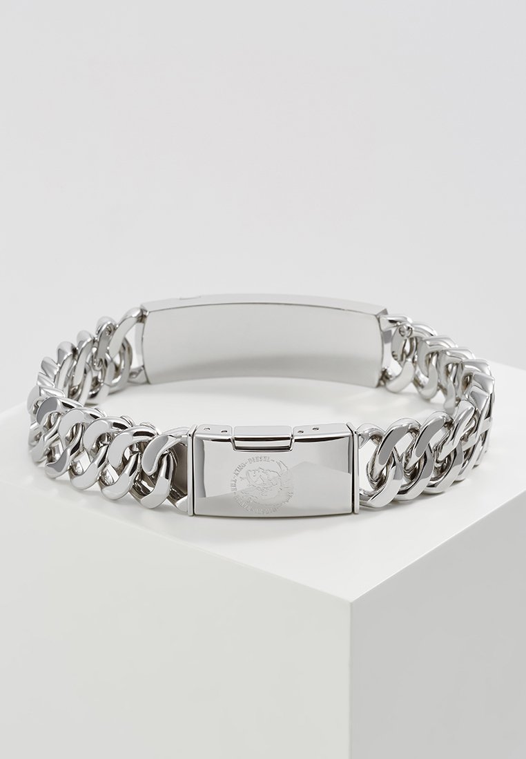 Bracelet en métal argenté avec un design de chaîne épaisse, texture lisse et fermoir rectangulaire avec des détails en relief.