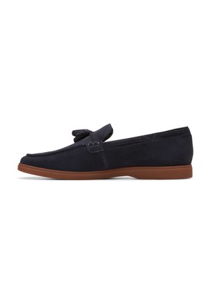 Mocasines de ante azul marino con suela plana de goma marrón, que presentan un nudo decorativo en la parte frontal y detalles de costura en los laterales.