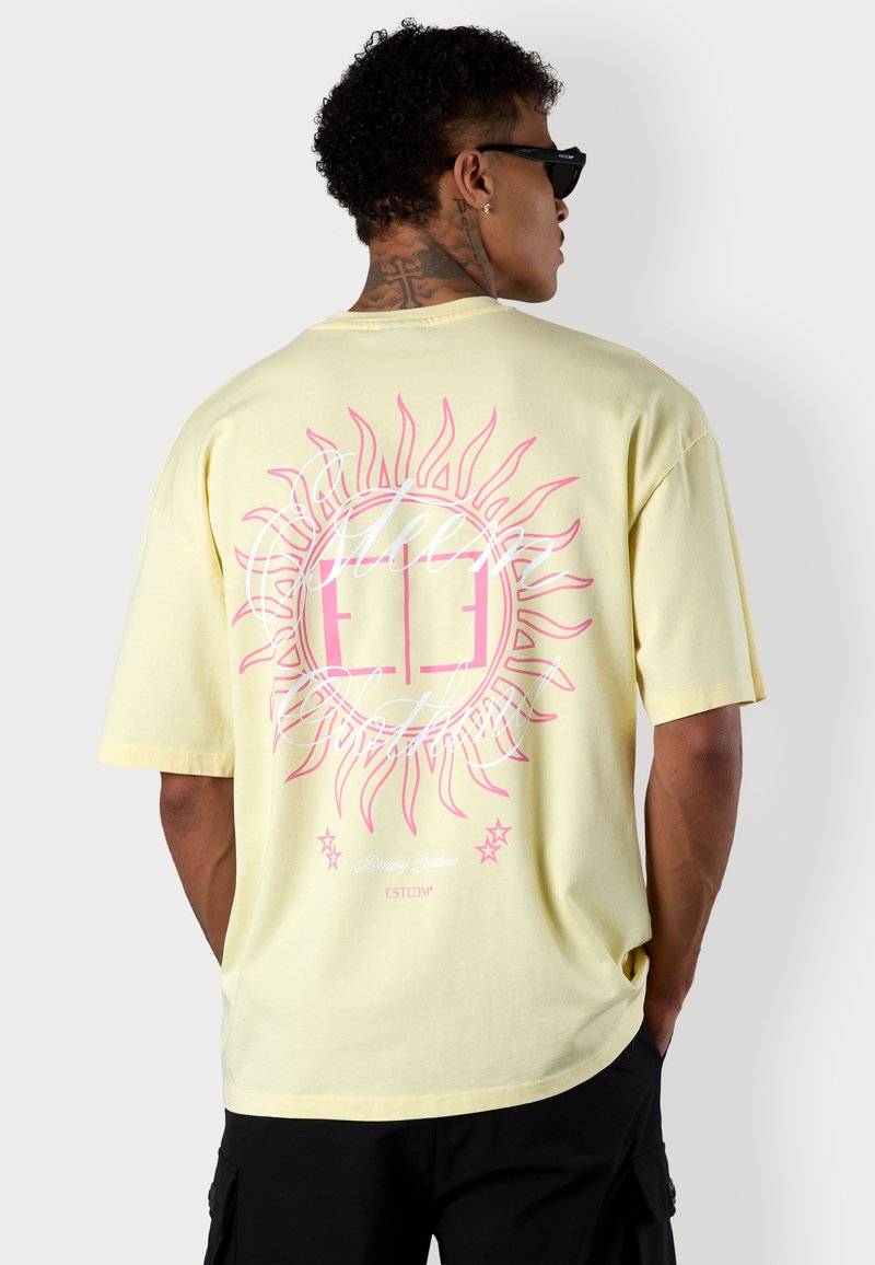 Gelbes Baumwoll-T-Shirt mit einem großen pinken Sonnenmotiv auf der Rückseite, mit dem Text "Blazing Sunshine" und dekorativen Sternen.