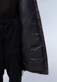 Zwarte pufferjack met een glad, glanzend oppervlak en een elastische trekkoordzoom. Gecombineerd met zwarte cargobroek met elastische taille en zijzakken.