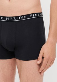 Black cotton boxer briefs with a thick branded waistband featuring "PIER ONE" in white text. Smooth texture, fitted design, and minimal stitching.