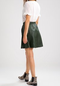 Zelená kožená sukně s hladkou texturou, nošená s bílým volánkovým topem s krátkým rukávem. Černé a béžové leopardí printové kotníkové boty.