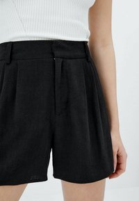 Pantaloni neri realizzati in tessuto testurizzato con vita alta, caratterizzati da plissettature frontali, tasche laterali e un orlo dritto.