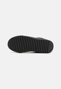 Czarna podeszwa sneakerów z rydżowym wzorem, o gładkim, zaokrąglonym kształcie i wytłoczonym tekstem marki wzdłuż krawędzi.