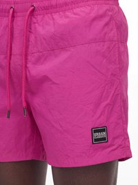 Felroze zwembroek met trekkoord in de taille en "Urban Classics" logopatch op het onderste linkerbeen, gedragen door een persoon.