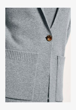 Hellgrauer Cardigan aus weichem Stoff. Verfügt über einen V-Ausschnitt, gerippte Bündchen und einen braunen Knopf. Zwei vordere Taschen mit leichtem Texturmuster.