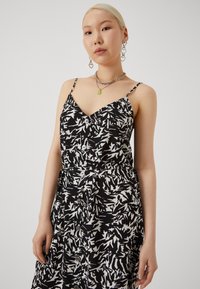 Rochie cu model alb și negru, cu bretele subțiri, decolteu în V, detalii cu nasturi pe față și talie strânsă.