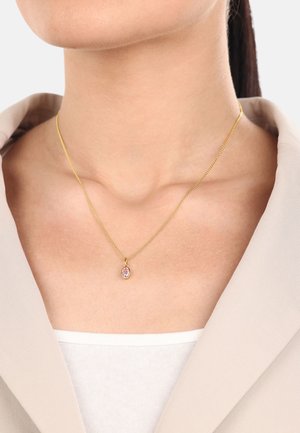 Goldene Kettenhalskette mit einem kleinen Anhänger, der mit einem lila Edelstein besetzt ist, getragen zu einem hellen Oberteil, das das Dekolleté betont.