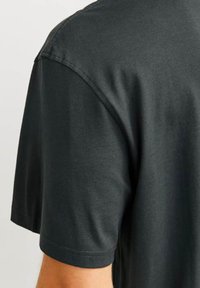 Camiseta de manga corta en gris oscuro, hecha de tela suave. Presenta un escote redondeado y costuras limpias en los hombros y el dobladillo.