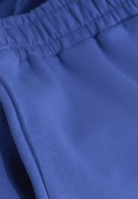 Niebieski elastyczny pas z gładkiego, lekkiego materiału, posiadający subtelny połysk i jednolitą fakturę. Widoczne detale szwów.