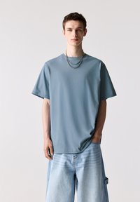 Lyseblå oversized t-shirt lavet af blødt stof, med korte ærmer, rund halsudskæring og parret med lyse denimshorts.