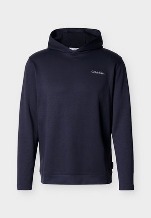 Tumesinise tooniga kapuutsiga pusa, millel on vasakul rinnal Calvin Kleini logo ja lõdva istuvusega, ühtlase taustaga.